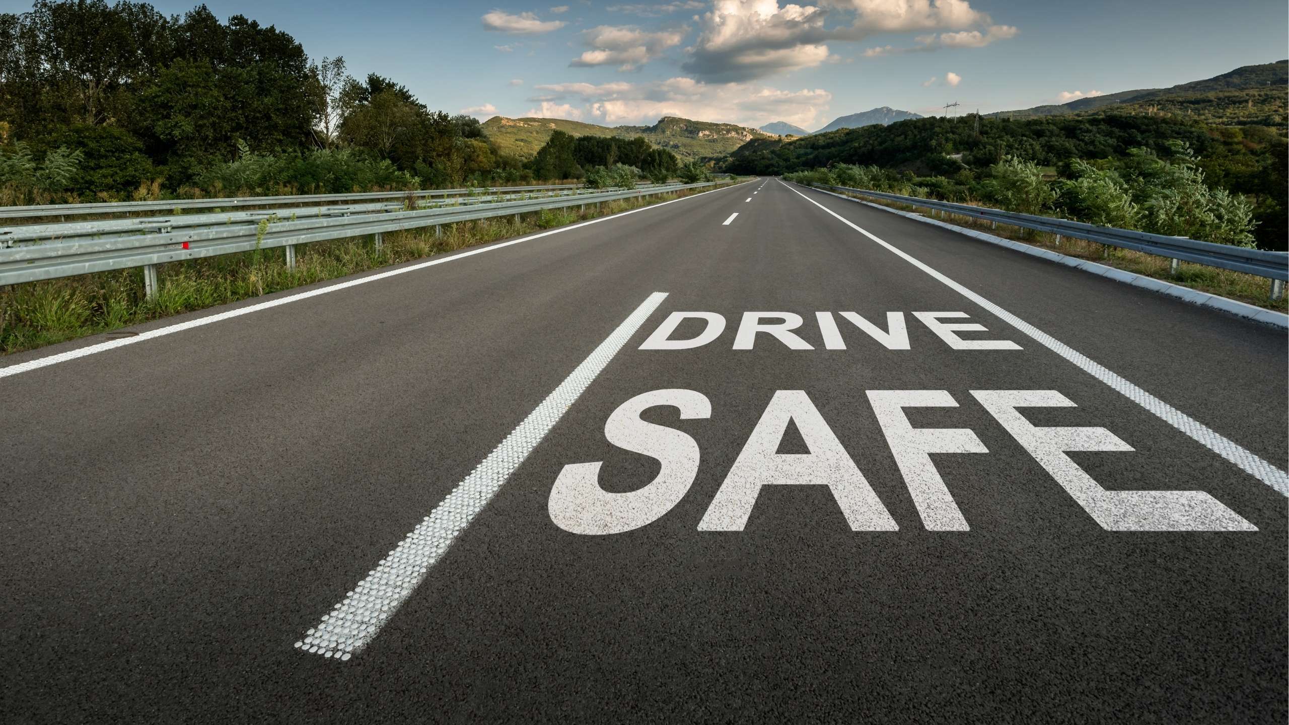 Open highway with mountains in the distance and the words “DRIVE SAFE” painted in large white letters on the road.