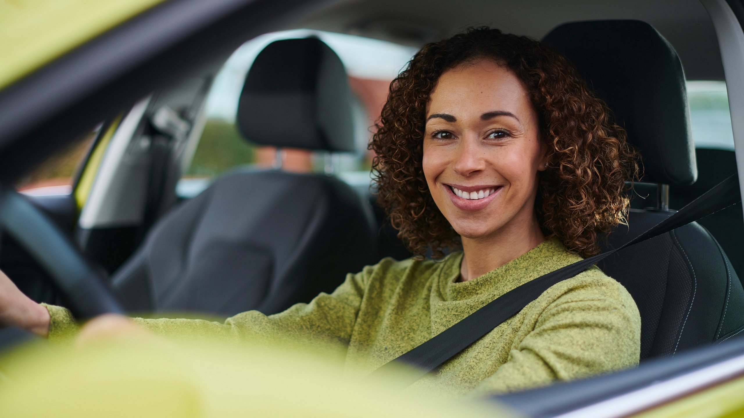 Woman sitting in the driver’s seat, smiling confidently while wearing a seatbelt during a driving lesson.
