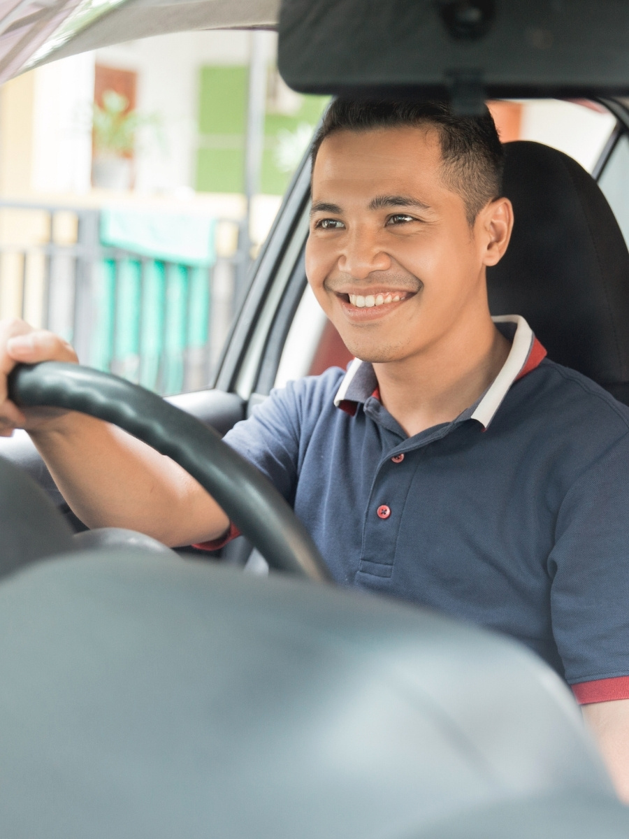 Smiling man sitting in the driver’s seat with both hands on the steering wheel during a driving lesson.