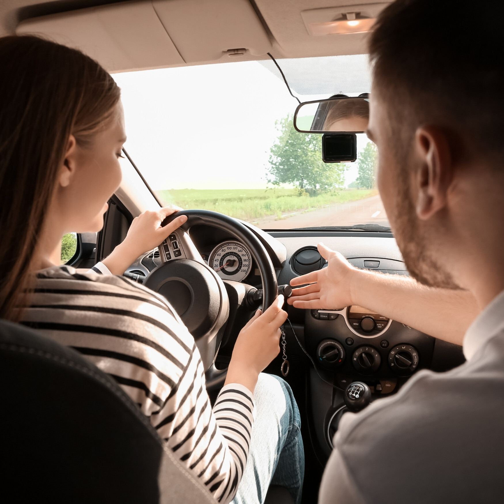 Driving instructor giving guidance to a student as she practices behind the wheel on a rural road.