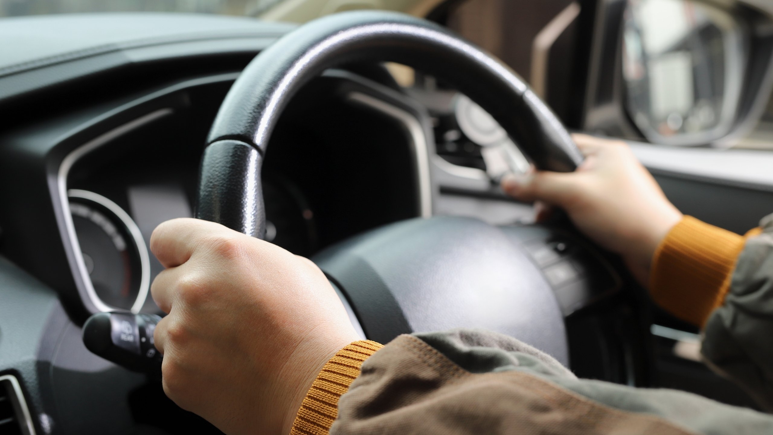 Close-up of a person holding a steering wheel with both hands while driving a car.