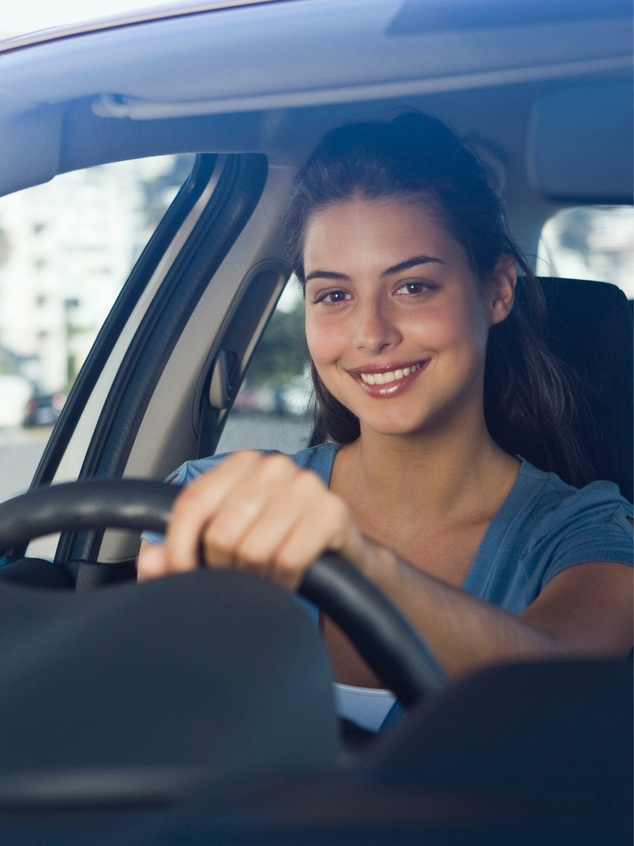 Female teen driver smiling while holding the steering wheel as she safely drives a car in texas.